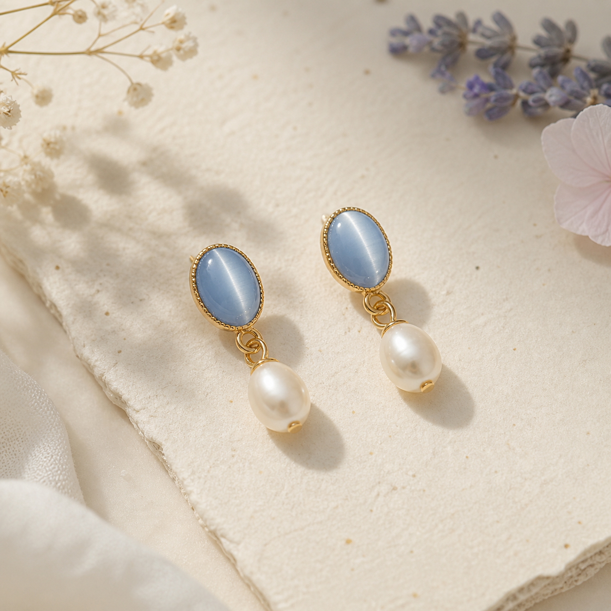 Minimalist pearl drop earrings with blue stone and gold setting on soft neutral background